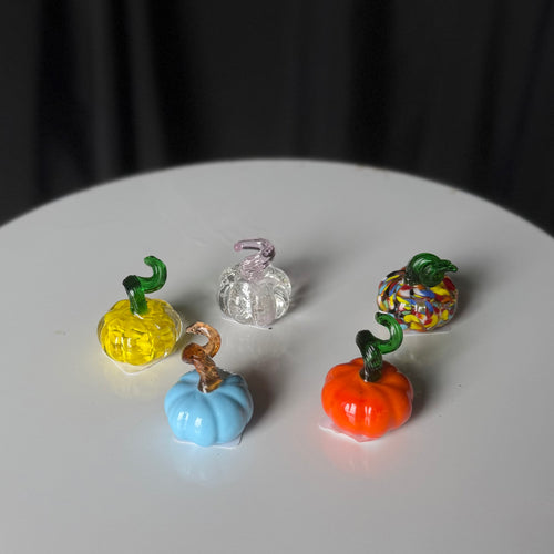 Tiny glass pumpkins in yellow, blue, orange, multicolored, and clear with a pink-tinted stem.