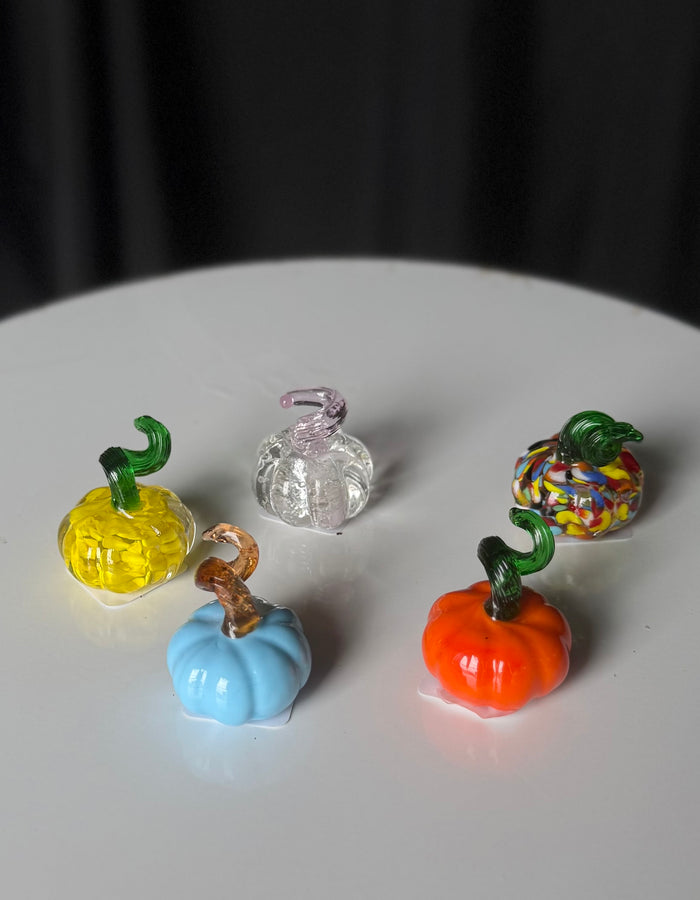 Tiny glass pumpkins in yellow, blue, orange, multicolored, and clear with a pink-tinted stem.