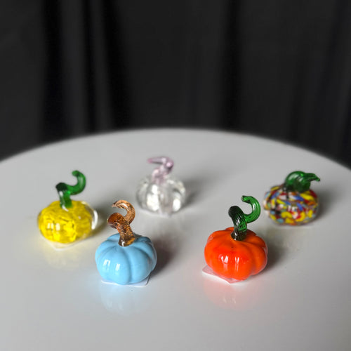 Tiny glass pumpkins with blue and orange pumpkins in the foreground and yellow, multicolored, and clear pumpkins behind.